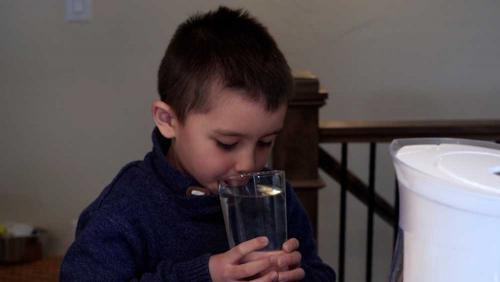 小孩从含铅水罐中倒水后，拿起水杯饮用。