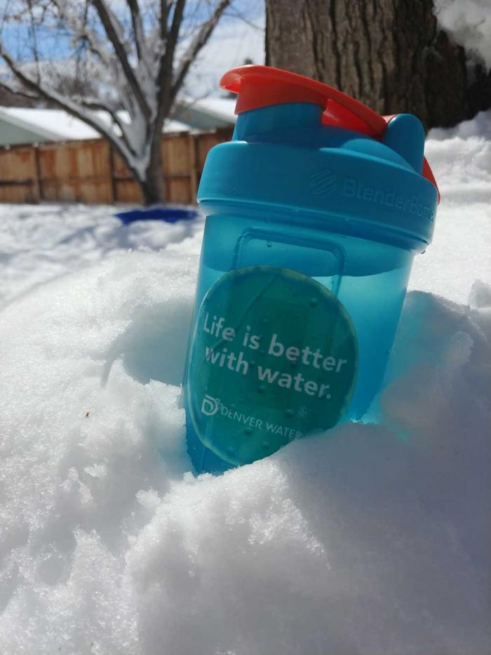 一个水瓶，用贴纸说“生活更好的水”和丹佛水徽标，在一堆雪中休息。