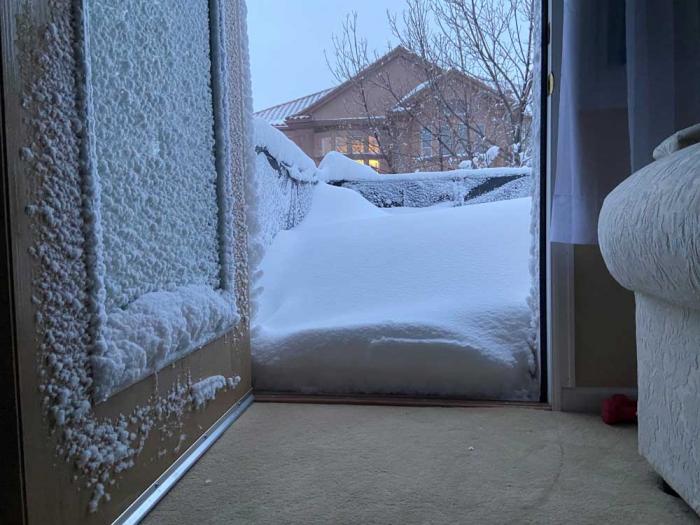 一个雪镶嵌的门打开到一个积雪覆盖的露台上，另一所房子在远处看到。