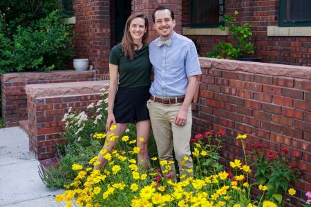 一个男人和一个女人站在一座低矮的砖墙前，脚下开着黄花。