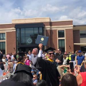 尼克头戴毕业帽，身穿毕业服，将学位举过头顶，笑容满面。