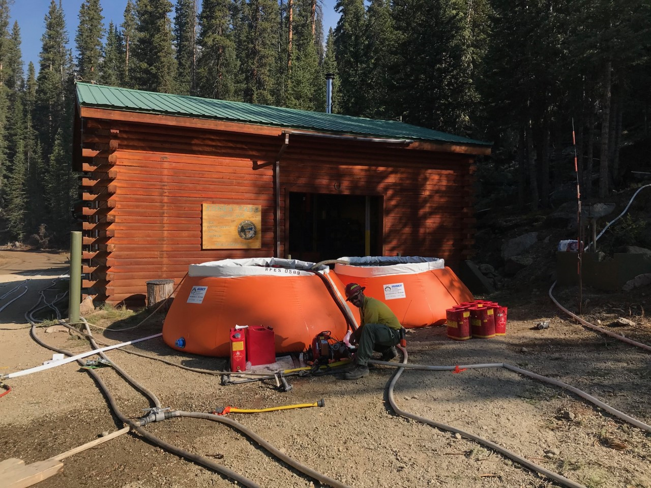 美国森林服务消防队员建立了一个储水罐，在丹佛水的Jone Pass设施围绕一座建筑物运行洒水器。照片信用：美国森林服务。