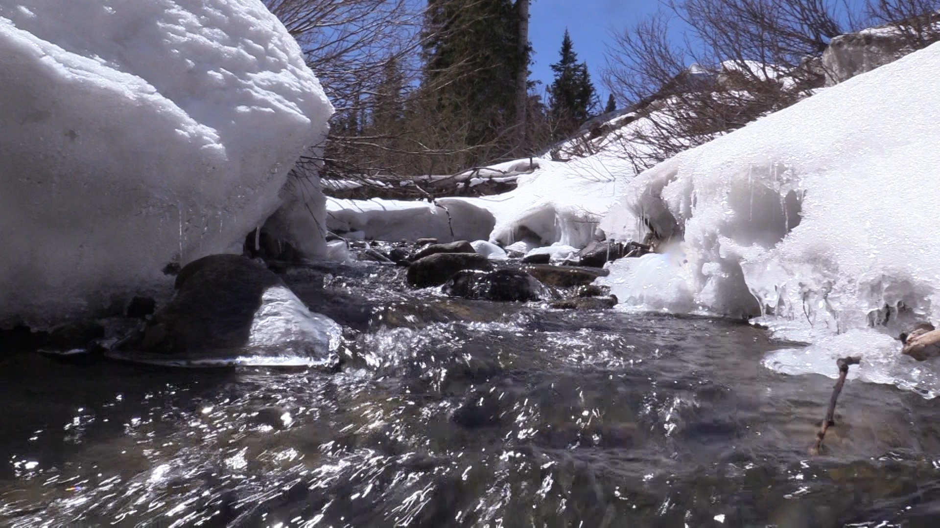 一堆堆的雪形成了一条小溪，溪水从岩石上流过。